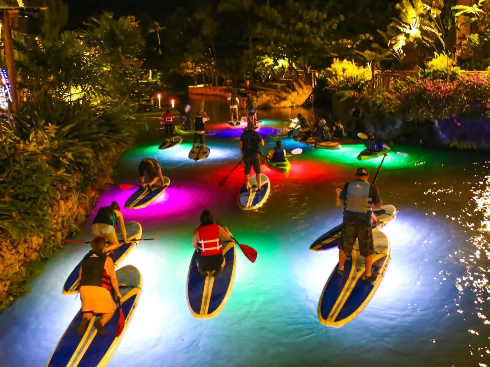 people paddle boarding in illuminated water at night
